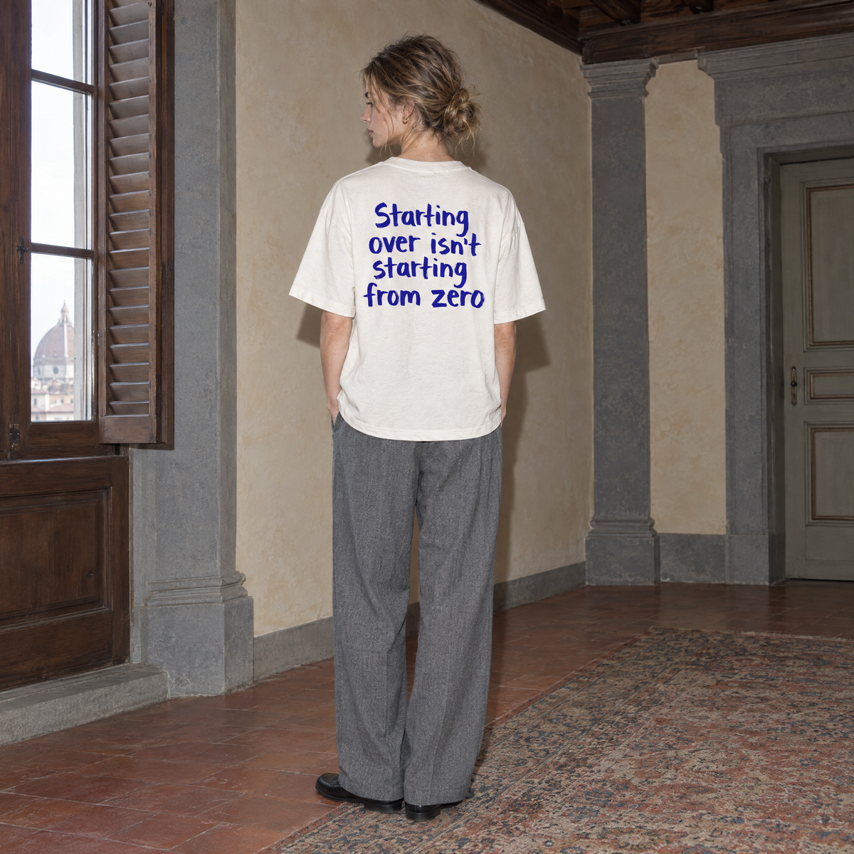 Woman wearing the white Start Over t-shirt from behind, blue brush-lettered back print reading Starting over isn't starting from zero
