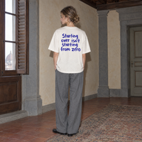 Woman wearing the white Start Over t-shirt from behind, blue brush-lettered back print reading Starting over isn't starting from zero