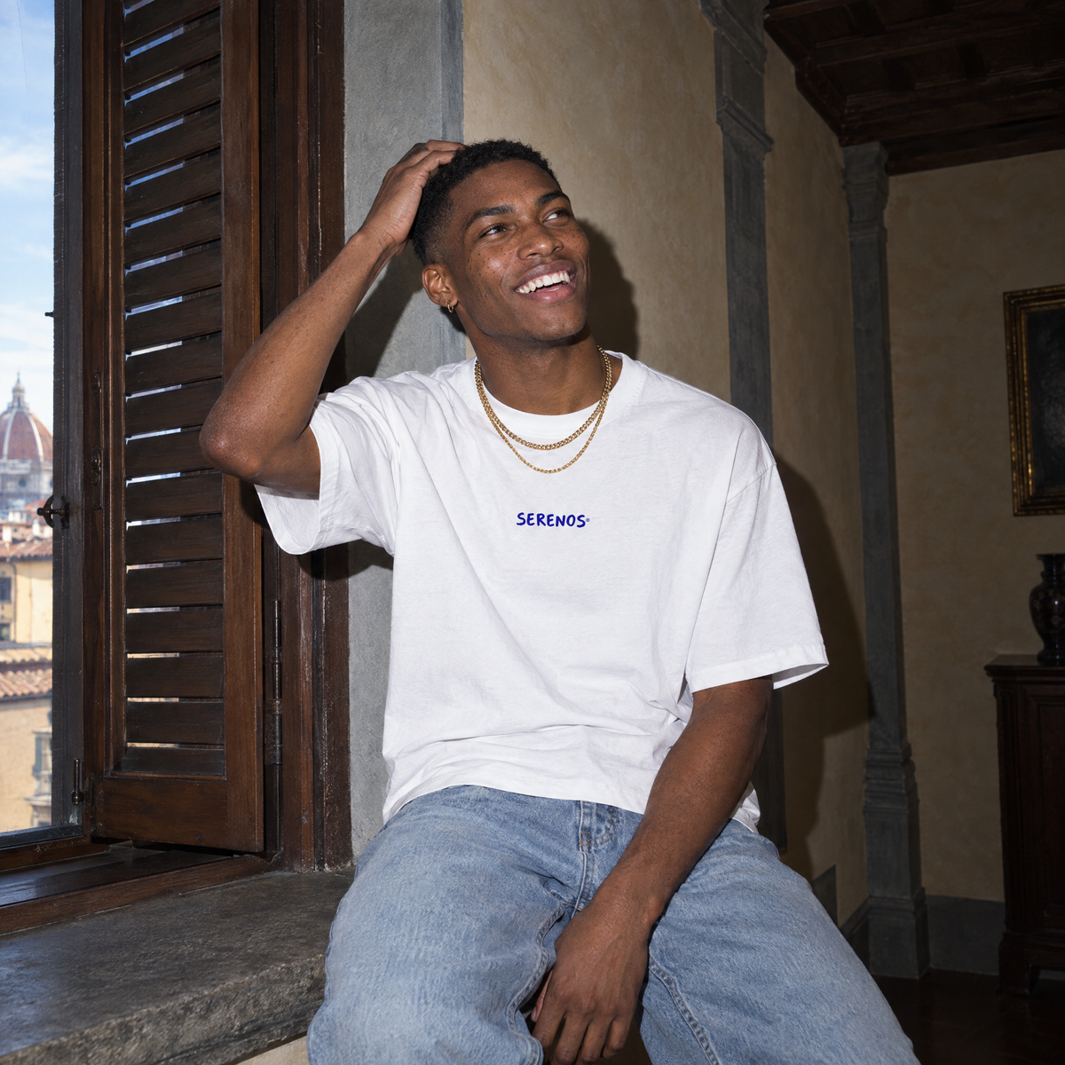 Man laughing on a window sill in a Florentine palazzo wearing the white Start Over t-shirt