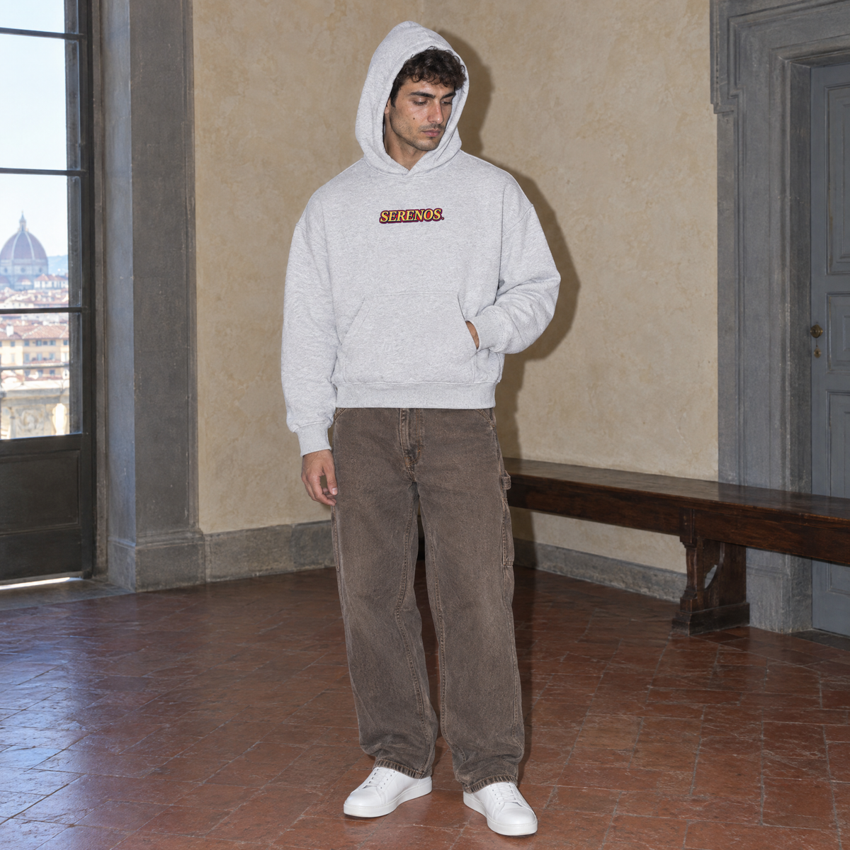 Man with the hood up wearing the SERENOS Success oversized boxy hoodie in flower gray in a Florentine palazzo room