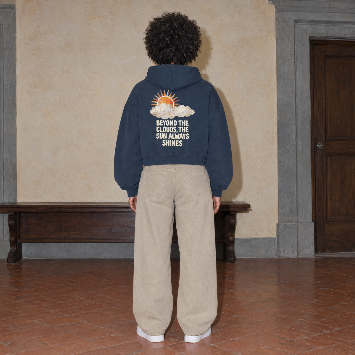 Woman seen from behind wearing the navy SERENOS Sun Above oversized boxy hoodie with the Beyond The Clouds The Sun Always Shines back print, cropped boxy fit