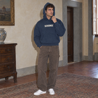 Man with the hood up wearing the navy SERENOS Sun Above boxy hoodie in a Florentine palazzo