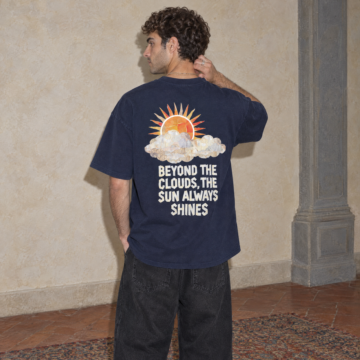 Man wearing the navy Sun Above oversized boxy t-shirt, seen from behind, back print reading Beyond the clouds, the sun always shines
