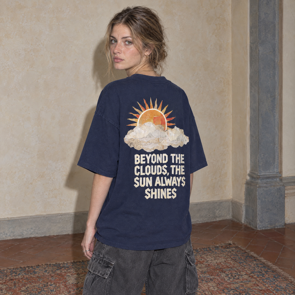 Woman wearing the navy Sun Above oversized boxy t-shirt, seen from behind, back print reading Beyond the clouds, the sun always shines