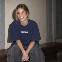 Woman laughing on a bench in a Florentine palazzo, wearing the navy Sun Above oversized boxy t-shirt by Serenos