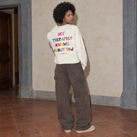 Woman seen from behind wearing the cream Therapist long sleeve by Serenos, back print reading my therapist knows about you