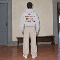 Man seen from behind wearing the SERENOS Therapist oversized boxy hoodie in flower gray, back print reading My therapist knows about you in multicoloured cut paper letters