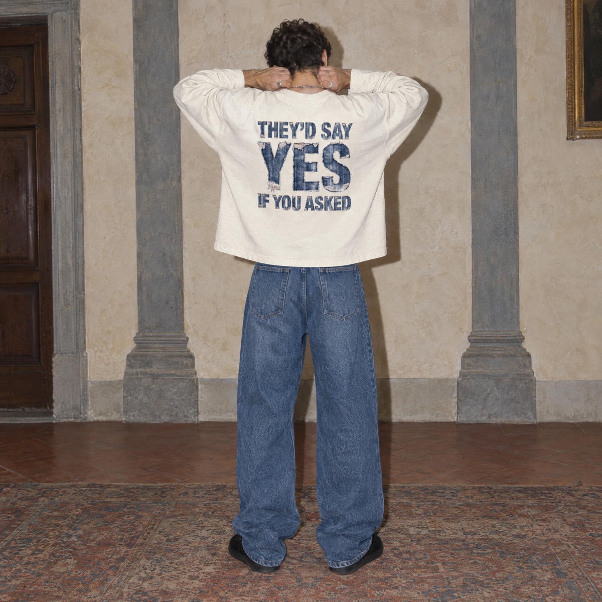 Man seen from behind wearing the cream Yes long sleeve by Serenos, denim texture back print reading they'd say yes if you asked