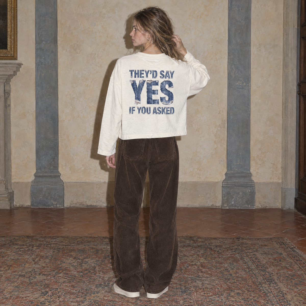 Woman seen from behind wearing the cream Yes long sleeve by Serenos, denim texture back print reading they'd say yes if you asked