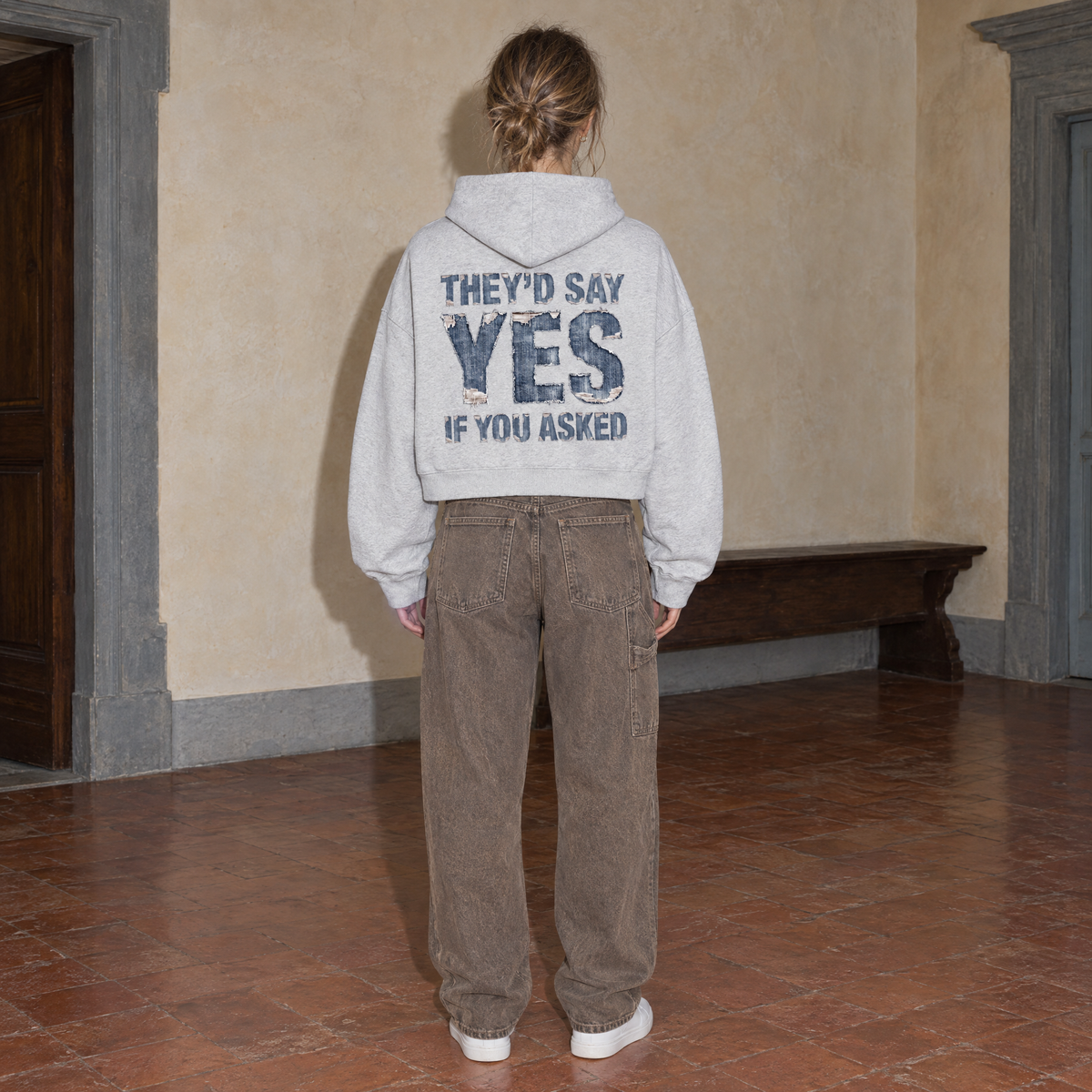 Woman wearing the SERENOS Yes oversized boxy hoodie in flower gray, seen from behind showing the They'd Say Yes If You Asked denim back print, cropped boxy fit