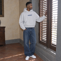 Man at a shuttered window wearing the SERENOS Yes oversized boxy hoodie in flower gray in a Florentine palazzo room