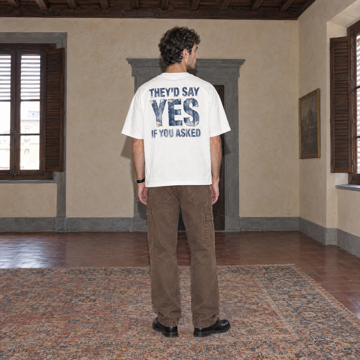 Man wearing the white Yes t-shirt from behind, denim-textured back print reading They'd say yes if you asked