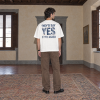 Man wearing the white Yes t-shirt from behind, denim-textured back print reading They'd say yes if you asked